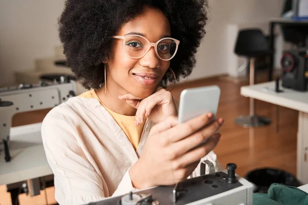 Donna seduta a controllare il suo smartphone durante la pausa dopo aver ricucito vecchi vestiti — Foto Stock