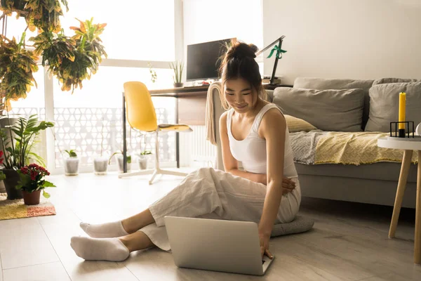 Chica freelancer sentada en el suelo mientras trabaja en el ordenador desde casa —  Fotos de Stock