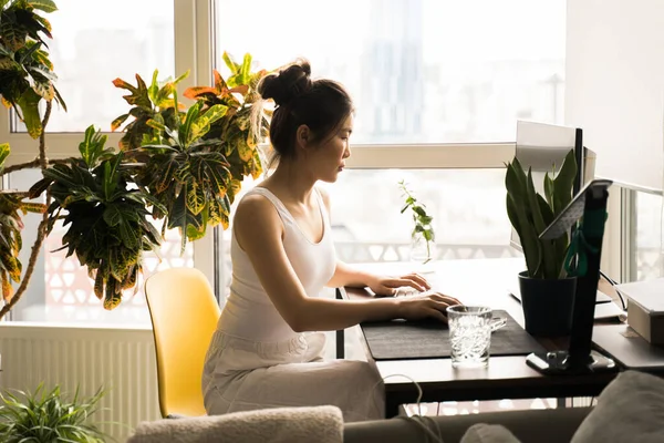 Vrouw die naar het computerscherm kijkt en typt terwijl ze aan tafel zit — Stockfoto