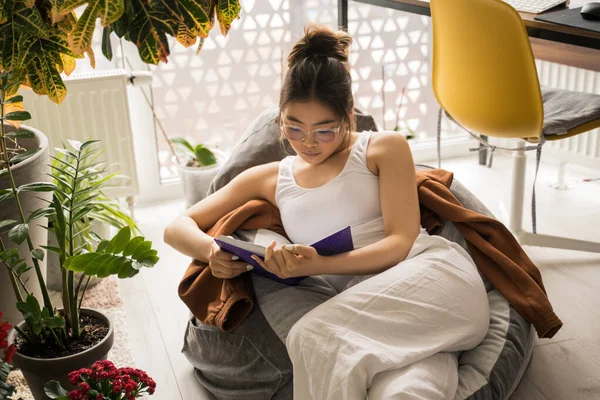 Chica multiracial sosteniendo el libro, mientras lee o estudia en casa —  Fotos de Stock