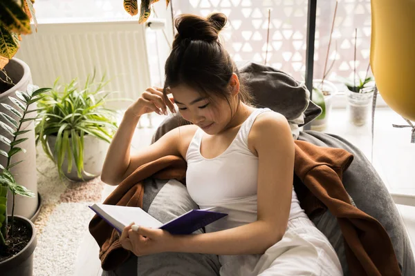 Lectura femenina, mientras descansa con emociones tranquilas en una silla suave en casa —  Fotos de Stock