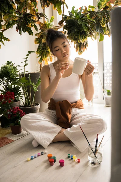 Mujer sosteniendo la taza mientras se prepara para pintar cuadros —  Fotos de Stock