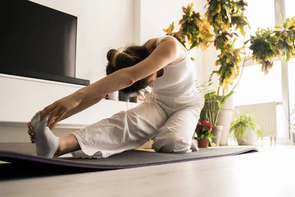 Frau in Sportbekleidung beim Stretching, während sie auf der Matte auf dem Boden sitzt — Stockfoto
