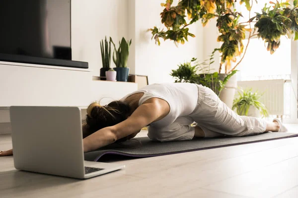 Frau streckt ihren Rücken beim Training auf der Matte vor dem Laptop — Stockfoto