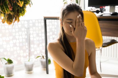 Bir gözünü saklayan bir kadın yoga yaparken bağdaş kurup yerde oturuyor.