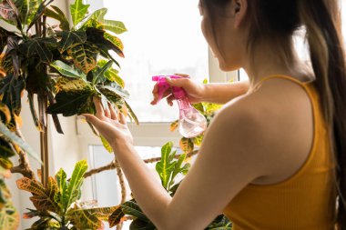 Çiçekçi elinde fıskiyeyle evde dikilip çiçekleriyle ilgileniyor.