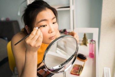 Kumral saçlı bir kadın masada otururken her gün makyaj yapıyor.