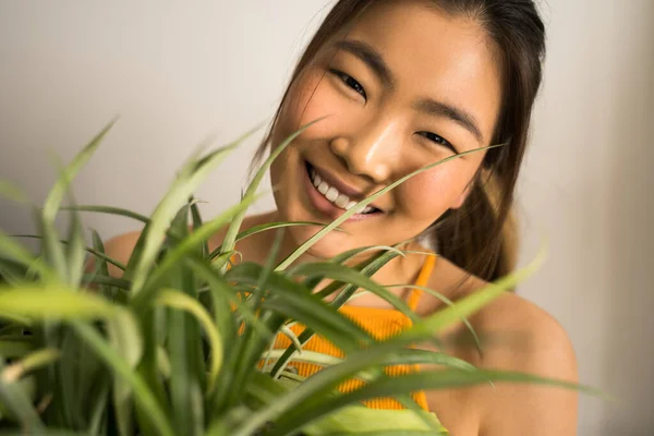 Donna sorridente e guardando la fotocamera mentre tiene in mano erba con fiori domestici — Foto Stock
