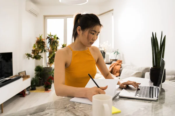 Vrouw zit aan de keukentafel en kijkt goed naar haar laptop — Stockfoto