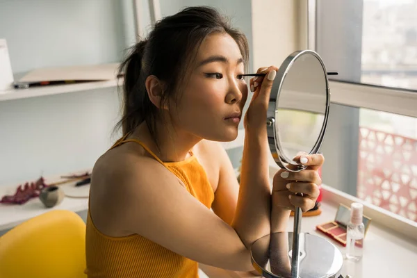 Donna con capelli castani che fa il trucco quotidiano a casa in camera da letto — Foto Stock