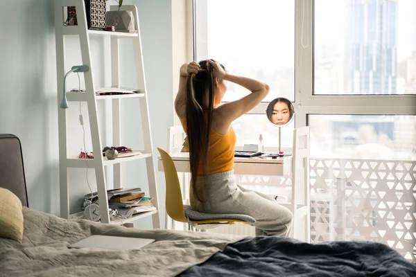 Mujer vestida con ropa doméstica mirando su reflejo mientras está sentada frente al espejo —  Fotos de Stock