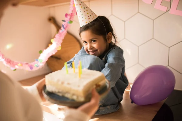 Girl looking at her birthday cake with candles while thinking about her wishes