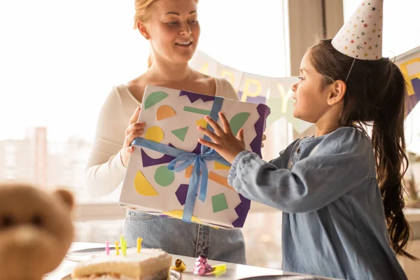 Woman giving a gift to her daughter wearing party cap while spending her birthday — Φωτογραφία Αρχείου