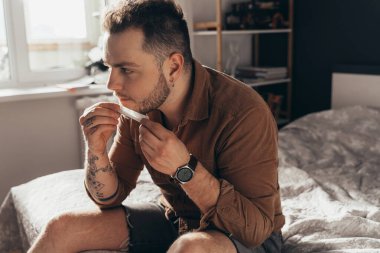 Masada oturan ve dili sarılmış esrar sigarasıyla yuvarlanan bir adam.