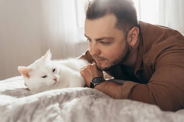 Man bonding to his white fluffy cat while spending time together at the bed — Photo