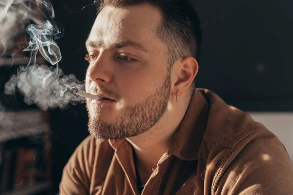 Man andas in en rök av handen rullade cigarett när man röker cannabis hemma — Stockfoto