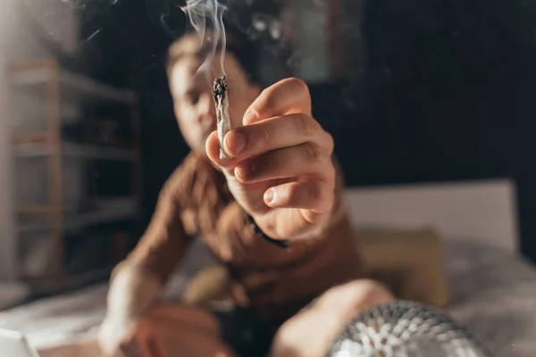 Man som erbjuder en handrullad cannabis cigarett sittande vid sängen — Stockfoto