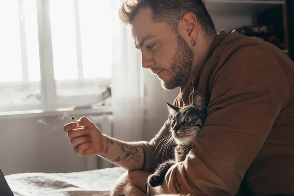 Hombre fumando cannabis y pasando tiempo con su gato mientras ve algo — Foto de Stock