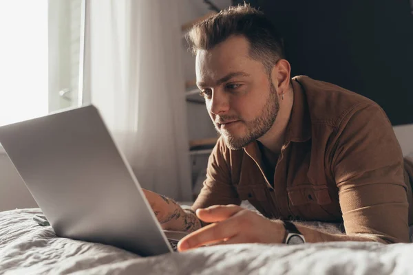 Hombre acostado en el estómago en la cama delante de la computadora portátil y trabajando — Foto de Stock