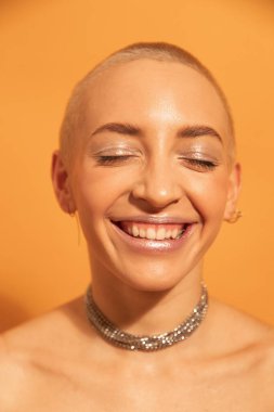 Kısa saçlı, beyaz bir kadın. Gözleri kapalı gülümsüyor.