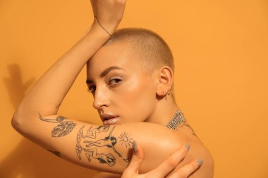 Dövmeli bir kadın yüzüne yakın poz veriyor ve kameraya bakıyor.