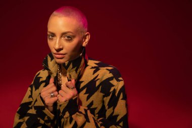 Şık bir palto giyen bir kadın şık poz verirken yakasını düzeltiyor.