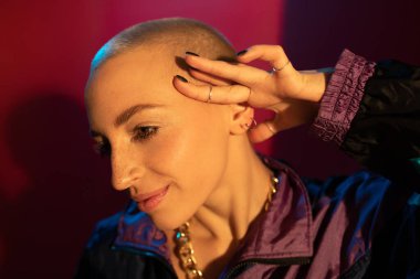 Kısa saçlı kadın kırmızı arka planda poz veriyor ve mutlu bir şekilde kenara bakıyor.