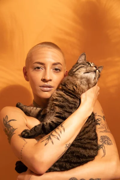 Woman posing in front of the yellow wall with her striped cat at the hands