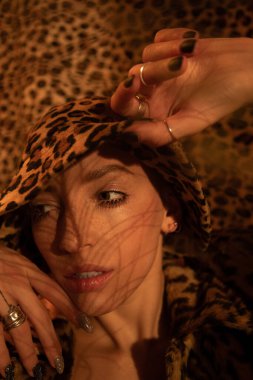 Leopar desenli panama giyen bir kadın yüzüne yakın el ele tutuşup gözlerini kaçırıyor.