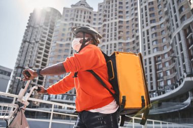 Yemek dağıtırken bisiklete binen koruyucu maskeli bir adam.