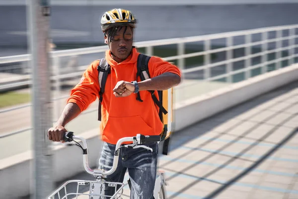 Парень в шлеме и сидит во время проверки велосипеда с помощью умных часов — стоковое фото