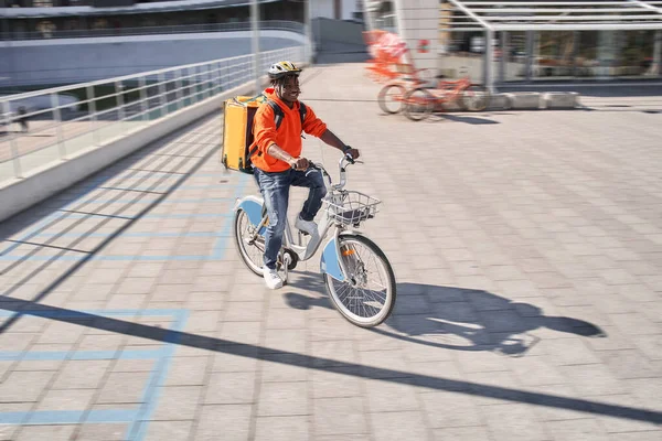 Leverans man bär röd tröja och gul leverans ryggsäck sitter på cykeln — Stockfoto