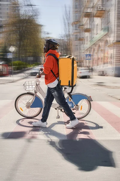 Courier man med stor gul ryggsäck korsning väg med cykeln — Stockfoto