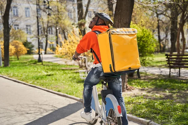 Курьер в тепловом рюкзаке едет на велосипеде по дороге — стоковое фото
