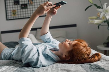 Kadın kameraya bakıyor ve selfie çekiyor, evde yatarken.