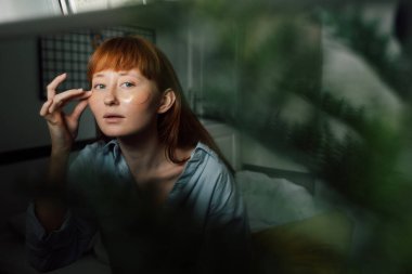 Göz bantlı bir kadın kendini izole ederken aynaya bakıyor.