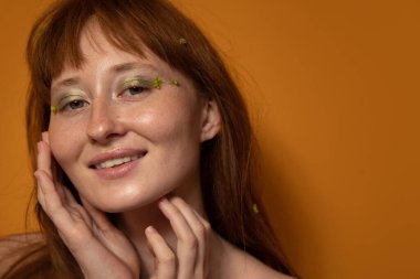 Çıplak omuzlu, güzel tenli, yüze dokunan ve gülen bir kadın.