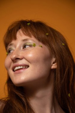 Kızıl saçlarına çiçekli bir kadın stüdyoda poz verirken gözlerini kaçırıyor.