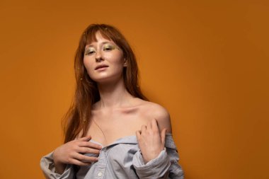 Çıplak makyajlı ve yeşil göz farı olan bir kadın muhteşem omuzlarına dokunuyor.