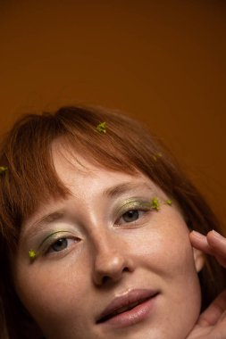 Çıplak omuzlu, güzel tenli, yüze dokunan ve gülümseyen bir kadın.