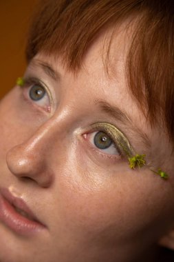 Çıplak makyajlı ve yüzünde yeşil göz farı olan güzel bir kadın.