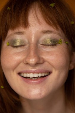 Kapalı gözlü kızıl kadın poz verirken yüksek sesle gülüyor.