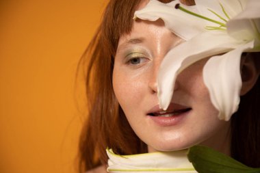 Yeşil gözlüklü bir kadın gözlerini zambağın arkasına gizliyor ve başka tarafa bakıyor.