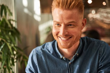 Kafede oturan ve dişlek gülüşlü birine bakan bir adam.