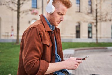 Kulaklık takan bir adam akıllı telefonuna bakıyor ve müzik dinliyor.