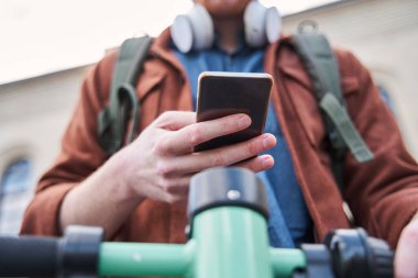 Adam motorlu scooter kullanıyor ve akıllı telefon kullanırken direksiyon tutuyor.