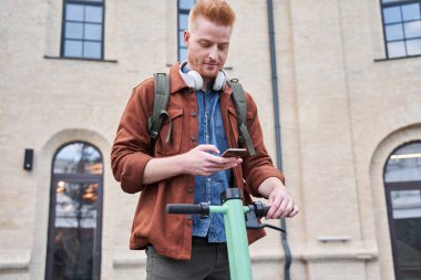 Cep telefonu tutan ve motorlu scooterıyla kilidi açan adam.