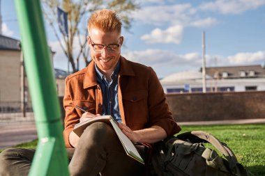 Doğada çalışırken gülümseyen ve notlar alan gözlüklü bir adam.