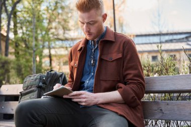 Adam bankta oturup çalışırken bazı notlar alıyor.