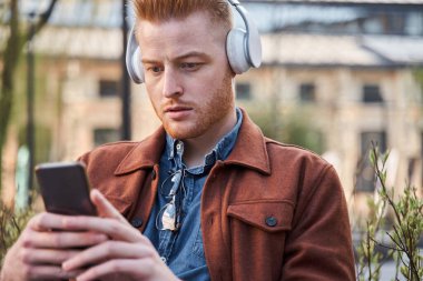 Kulaklık takan bir adam sokakta bankta oturmuş müzik dinliyor.